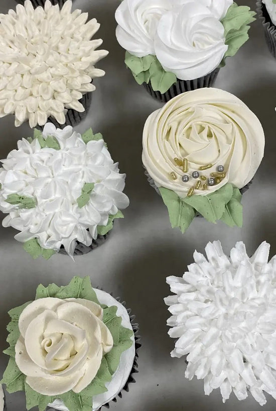 Decorative cupcakes with white frosting and green accents on a metal surface